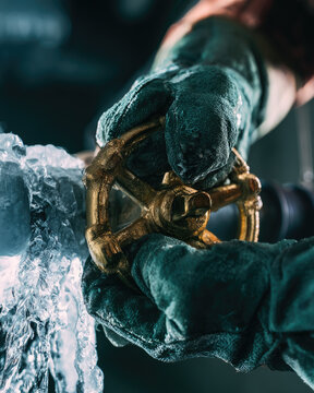 Frozen water pipe burst with gloved hands turning brass shutoff valve during urgent plumbing maintenance in cold basement light