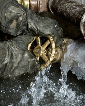 Frozen water pipe burst, gloved hand, brass shutoff valve, leaking pipe repair under urgent basement conditions