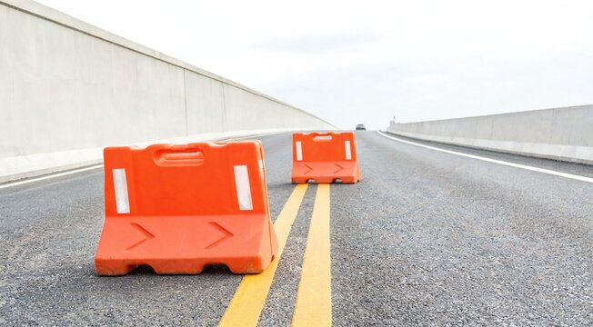 Two orange traffic barriers on a deserted road with double yellow lines. The sky is overcast, creating a somber atmosphere.