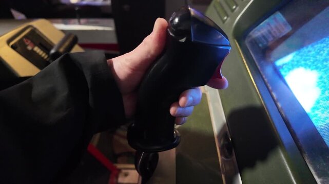 Hand gripping and pressing buttons on vintage arcade game joystick in dim room