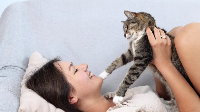 Woman playfully holds trusted cat above her while smiling. Relaxed feline stretches its paws outward during a joyful moment of shared affection.