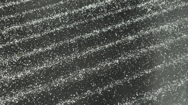 Small snowflakes gently fall onto a dark roof, creating a natural winter outdoor scene.
