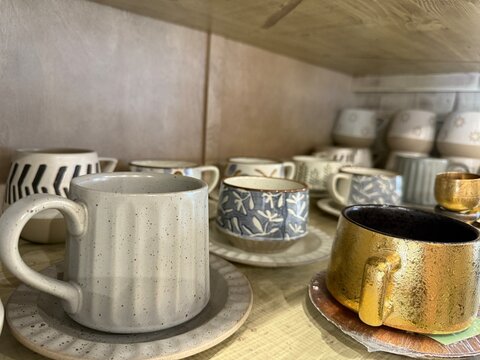 Various ceramic mugs and saucers on a wooden shelf in a cozy setting as display background