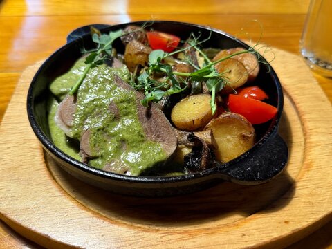 Gourmet dish of roasted potatoes, beef slices, green sauce, and vegetables in a skillet