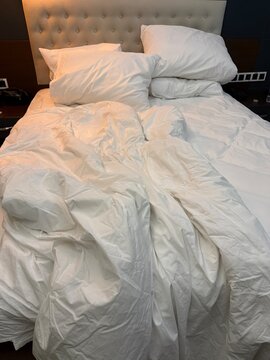 Unmade bed with crumpled white bedding in warm light, ideal for relaxation themes or background