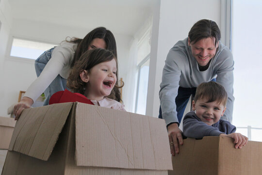 Happy parents having fun pushing their laughing children in cardboard boxes while moving into a new home.