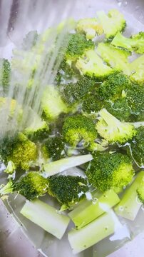 Blanching fresh green broccoli in a pan of boiling water, vertical video