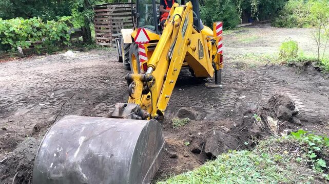 Yellow excavator bucket scooping soil and digging trench close up, ground preparation process, site excavation.