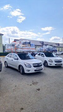 Two white Chevrolet Cobalt sedans with heavily loaded roof racks parked in Karabutak; long-distance luggage transport; Aktobe, Kazakhstan 10.08.25
