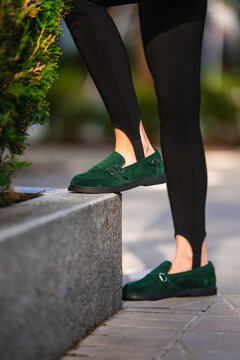 person wearing green loafers standing on stone block in casual urban setting with plants and paved ground close-up focusing on lower legs and shoes. casual and stylish.