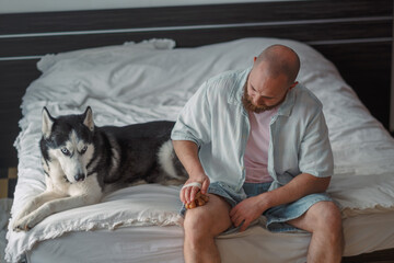 Man sitting on a bed with a massager next to his husky © iwavephoto