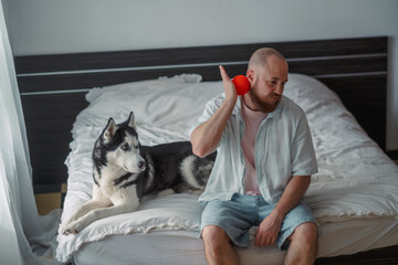 Man massaging his neck with a ball next to his husky © iwavephoto