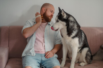 Man with a wooden massager facing his husky on a sofa © iwavephoto