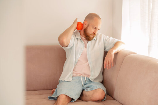 Man rolling a massage ball over a stiff neck at home