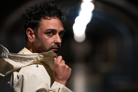 Portrait of a stylish man with spiky dark hair and beard glancing over his shoulder, dramatic backlighting, moody urban atmosphere