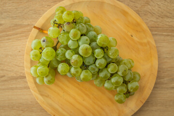 Fototapeta premium Fresh green grapes on a round wooden plate, shot from above on a light wood surface. Perfect for healthy eating and organic food concepts