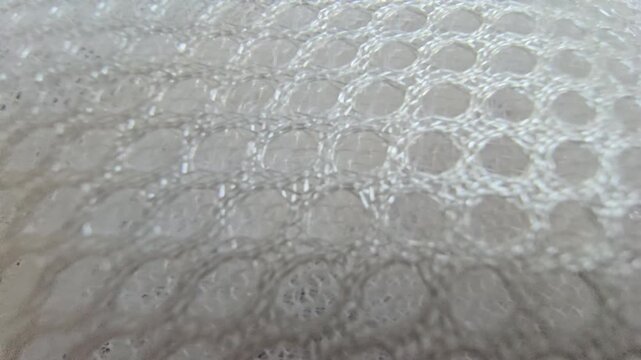 Macro close-up shot of white synthetic spacer mesh fabric. Detailed texture of breathable athletic air mesh material background, featuring a perforated honeycomb pattern and soft padded structure.