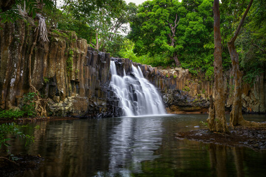 Rochester Falls in Mauritius flowing over distinctive basalt rock columns into a calm pool, surrounded by dense tropical forest and lush greenery.