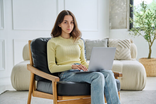 Young 18 years old woman with laptop sitting in armchair looking at camera