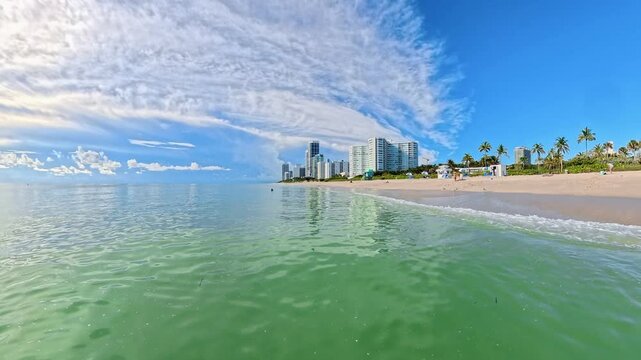 Wide coastal view shows beach hotels beyond gentle waves in Miami Florida.
