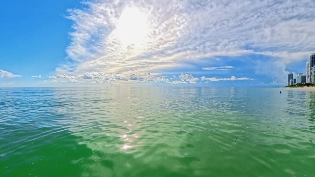 Ocean panorama reveals sandy shore, waterfront towers, and dramatic summer clouds.
