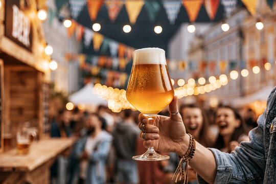 Hand raising beer glass at outdoor street festival with bunting flags and lights, Oktoberfest photo