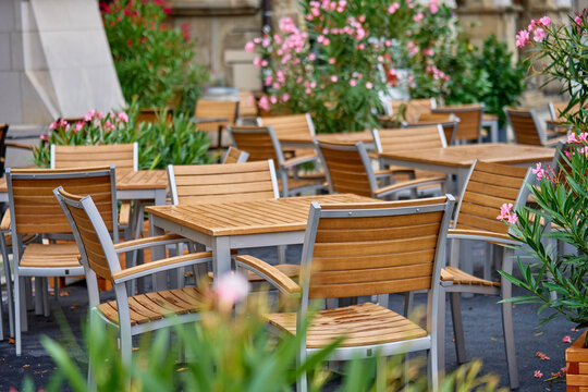 Empty outdoor cafe terrace with wooden tables and chairs surrounded by flowering plants