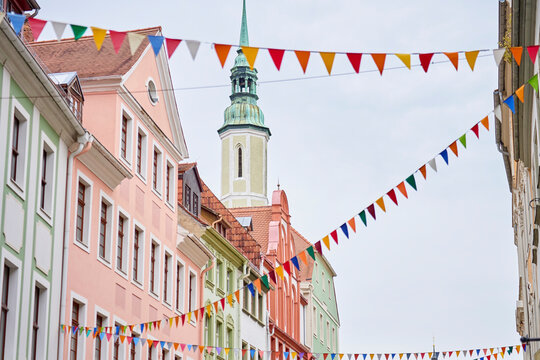 Historic street lined with colorful buildings, tiled roofs and church tower under festive bunting
