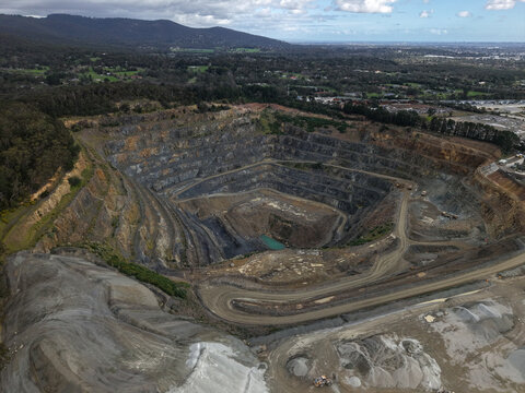 Montrose, Australia - 26 August 2026: Aerial view of Boral Montrose quarry showing deep terraced excavation pits, gravel piles, and surrounding forested hills under a bright sky.