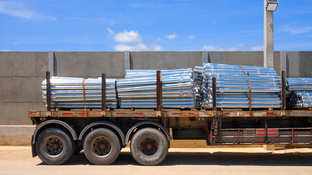 Galvanized steel pipes loaded on a heavy truck trailer for construction site delivery under blue sky, logistics and industrial transport concept.