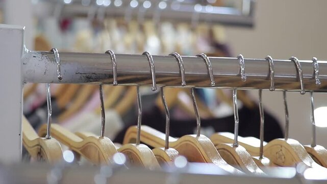 Row of wooden hangers hanging on a silver metal clothing rack in a boutique retail store or fashion showroom environment