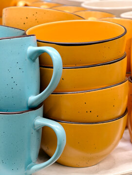 Blue cups and yellow deep ceramic plates displayed in grocery store shelving creating a practical kitchenware collection suitable for everyday dining and home use