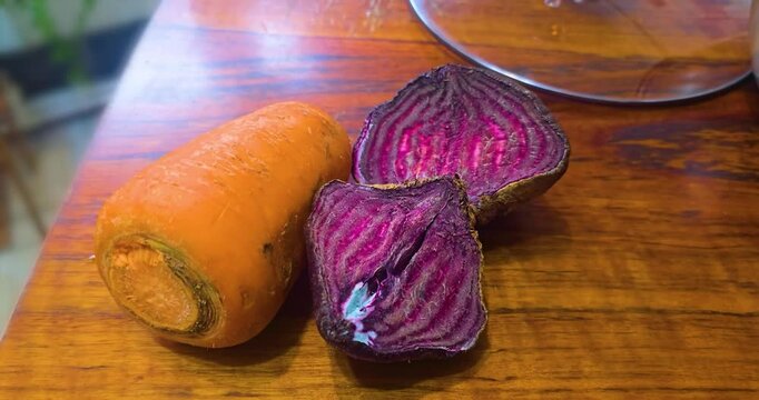 A carrot and two halves of a beetroot lie on a wooden table.