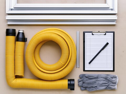 A collection of tools and equipment laid out on a flat surface, including yellow flexible tubing, a metal frame, a clipboard with a pen, and a pair of work gloves