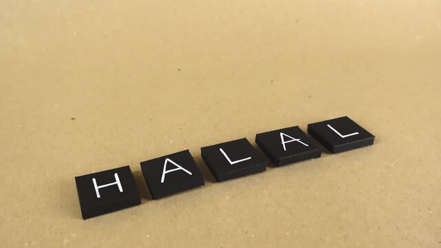 Black tiles with white letters spelling the word Halal, representing Islamic dietary law and permissible food for Muslims, on a light brown background with a smooth camera pan