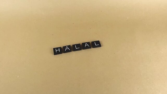 Black letter tiles forming the word halal slowly gliding across a light brown paper background, representing Islamic dietary law, permissible products, and cultural food certification