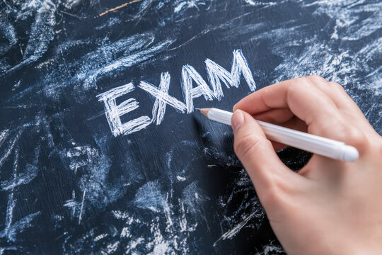 Hand writing exam word on blackboard with chalk