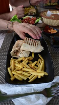 Marrakech, morocco. August 8, 2026. Close up of a person's hands taking a piece of traditional moroccan shawarma wrap from a plate with french fries in a local restaurant