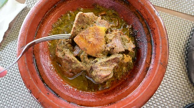 Marrakech, morocco. August 8, 2026. Traditional moroccan lamb tagine steaming in a classic terracotta clay pot. A person uses a fork to eat the tender, slow cooked meat