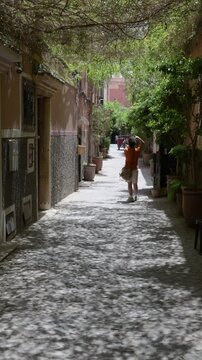 Marrakech, morocco. August 8, 2026. Young man exploring a beautiful alley in the old city of marrakech, morocco. Green vegetation covers the street, creating sun shadows