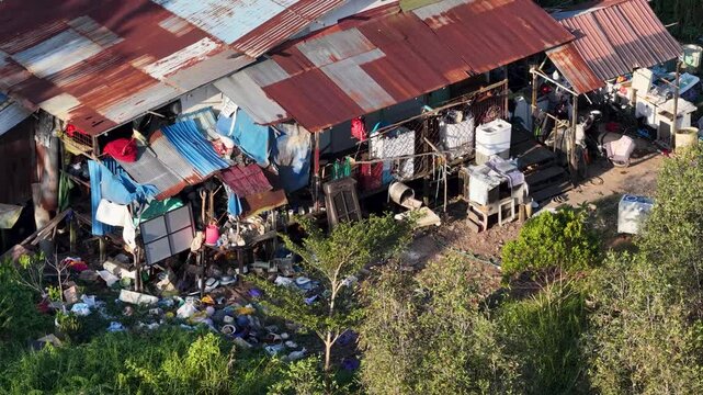 High angle view of a rustic wooden dwelling situated near trees with household trash on the ground