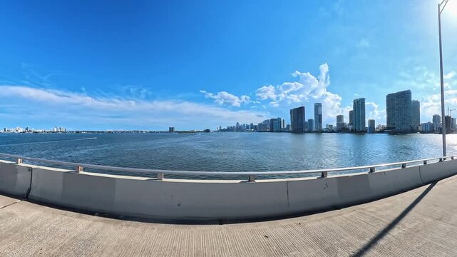  Camera travels beside waterfront towers and open bay under a sunny sky Miami.
