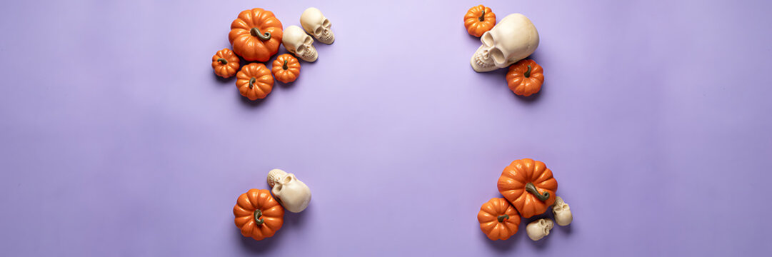 Four corner clusters of orange pumpkins and white human skulls arranged on a light purple background, for a festive, halloween celebration