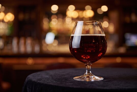 Snifter glass of dark craft beer in atmospheric pub interior bokeh