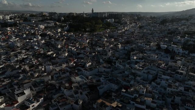 Wide aerial view of dense white neighborhoods spreading across a hilly city in Northern Morocco, revealing traditional urban fabric, mosque minaret and distinctive North African architecture.