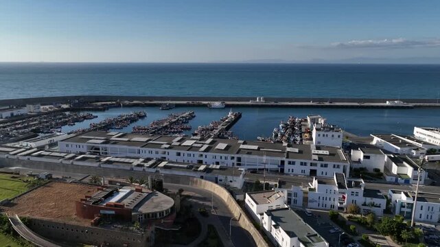 Aerial view of Tangier fishing port complex in Morocco, showing waterfront buildings, internal roads, harbor facilities, fishing piers and a protected basin beside the open sea.