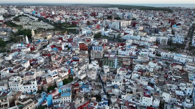 Wide aerial view over Asilah, Morocco, showing dense residential neighborhoods, traditional white and blue buildings, narrow streets and the compact urban fabric of this historic North African city.