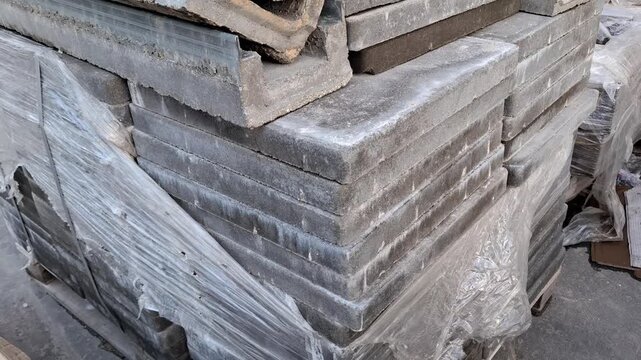 Concrete drainage channels and stone slabs stacked on a pallet outdoors, construction materials, building supply, infrastructure development.