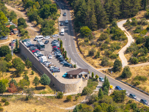 Komuna e Ohrit, North Macedonia - 11 August 2026: Aerial view of The Bay of Bones Museum parking area with cars and a bus, surrounded by trees and dry vegetation.