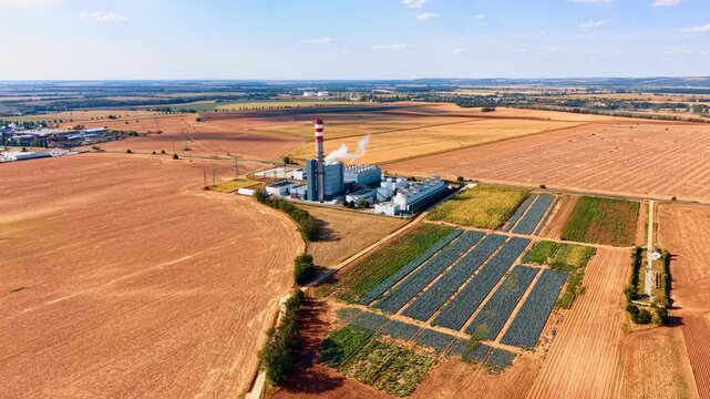 Approaching the industrial plant in the agricultural fields. Drone footage over the farmlands on sunny day.